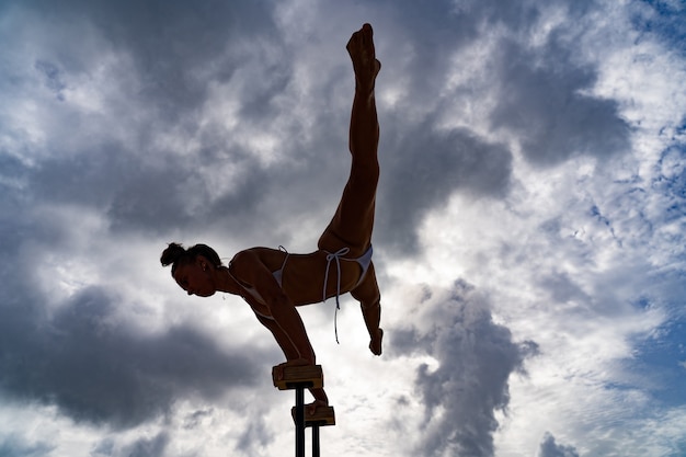 Artista de circo femenina flexible haciendo pino contra el increíble concepto de pasión y logro de motivación de cloudscape