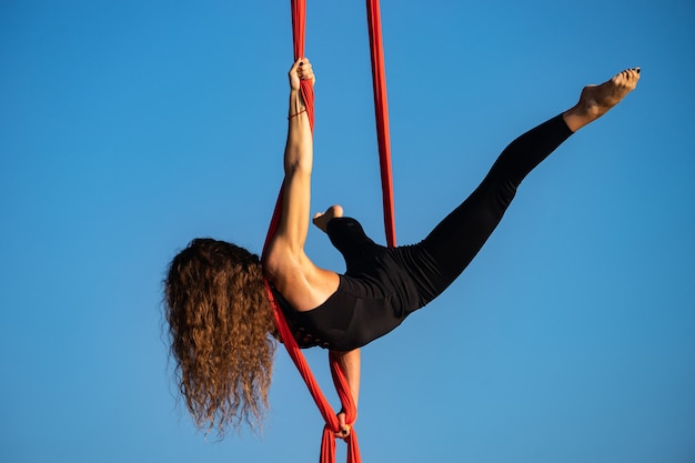 Artista de circo femenina hermosa y flexible bailando con seda aérea