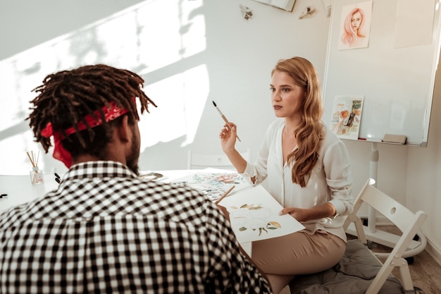 Artista com pincel. Artista criativa de cabelos loiros segurando uma escova de pintura enquanto ensina seus alunos