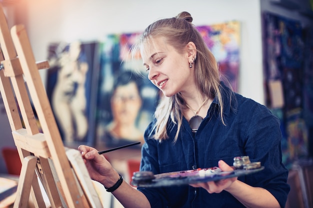 Artista da jovem mulher que trabalha na pintura no estúdio.