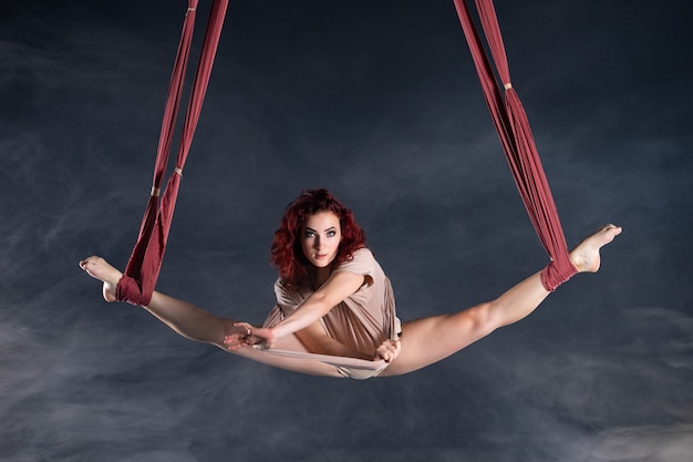 Artista de circo aéreo atlética, sexy e flexível feminina com a ruiva dançando no ar na seda.