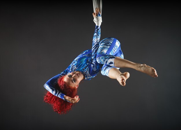 Foto artista de circo aéreo sexy atlético com ruiva em traje azul dançando no ar com equilíbrio.