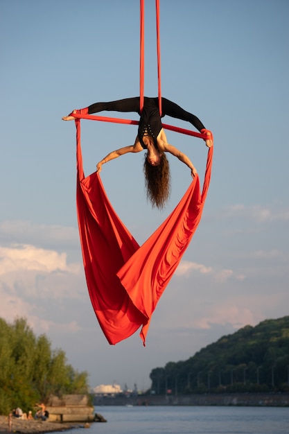 Foto artista de circo feminino bonita e flexível dançando com seda aérea em um céu.