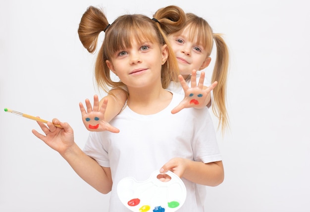 Artista de duas irmãs pequenas meninas legais com paleta de tintas em aquarela e pincel na mão, isolado no fundo branco. boa ilustração para passatempo infantil