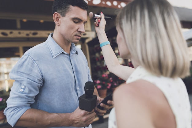 Artista de make-up fazendo maquiagem, jornalista que olha no telefone.