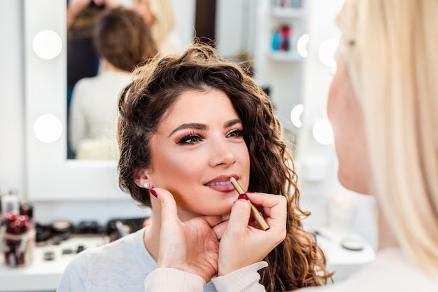 Artista de maquiagem aplicando maquiagem profissional em mulher jovem e bonita.