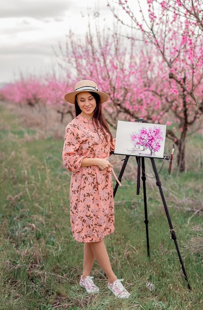 Artista de menina pinta um pomar de pêssego em uma primavera de pomar de pêssego