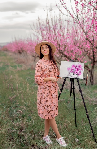 Artista de menina pinta um pomar de pêssego em uma primavera de pomar de pêssego