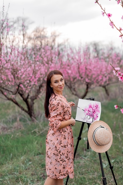 Artista de menina pinta um pomar de pêssego em uma primavera de pomar de pêssego