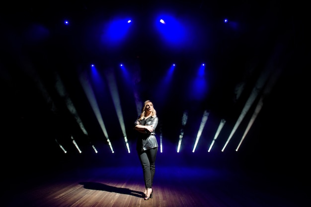 Artista de mulher bonita sobre o fundo de holofotes borradas no palco