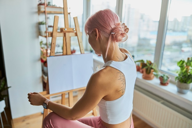 Artista de mulher elegante sentada no cavalete com uma tela em branco em casa