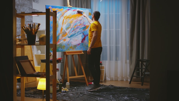 Artista de sucesso pintando com rolo em uma tela grande na oficina de arte.