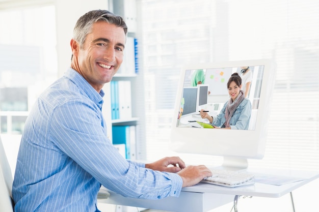Artista desenhando algo no tablet gráfico com colegas atrás contra homem sorridente digitando no teclado e olhando para a câmera