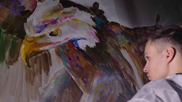 Artista designer desenha uma águia na parede Artesão decorador pinta um quadro com cor de óleo acrílico Pintor pintor vestido com uma camada de tinta Interior Aparência cinematográfica de magia negra