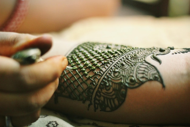 Artista dibujando un tatuaje de henna en la mano recortada de la novia