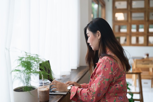 Artista diseñador gráfico femenino usando laptop trabajando en el alféizar de la ventana en el café