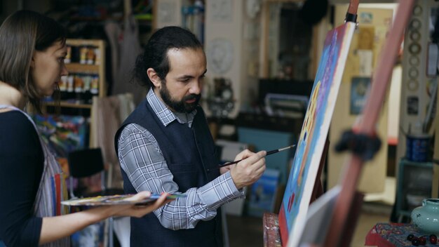 Un artista experto enseñando a una joven a dibujar pinturas y conceptos básicos de luz en un estudio de arte