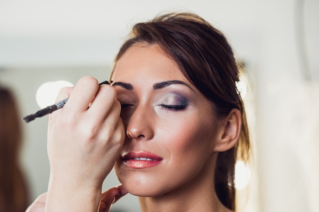 Artista fazendo maquiagem profissional de mulher jovem e bonita.