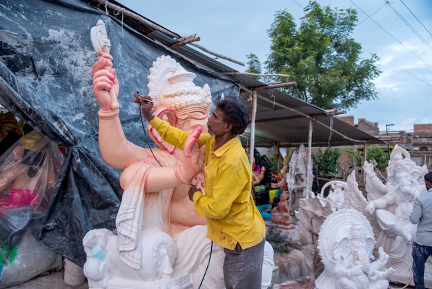 Artista fazendo uma estátua e dá os retoques finais em um ídolo do deus hindu Lord Ganesha em uma oficina de artista para o festival Ganesha