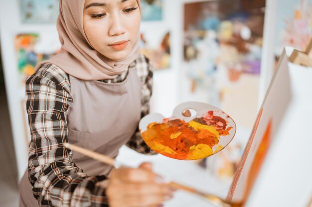 Artista femenina musulmana asiática concentrada pintando sobre lienzo