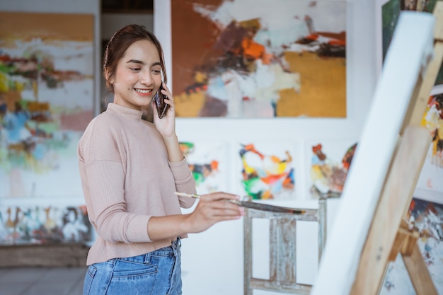 Artista femenina pintando sobre lienzo mientras habla por su teléfono