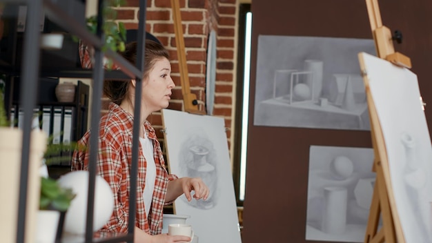 Artista femenina que usa un modelo de jarrón para explicar la técnica de dibujo, enseñando a los estudiantes a usar la creatividad y la imaginación. Taller práctico para dibujar boceto profesional sobre lienzo. Disparo de mano