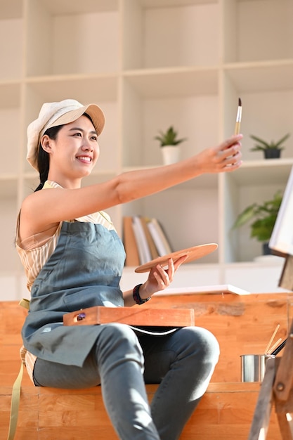 Artista femenina sentada frente al lienzo en el estudio de arte y pintura con acuarela.