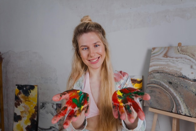 Artista femenina talentosa sonriendo feliz mostrando manos pintadas de colores.