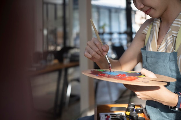 Artista femenina de tiro recortado sosteniendo un pincel y mezcla de pintura al óleo de color en la paleta.