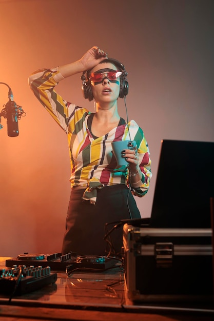 Foto artista feminina cansada bebendo café e bocejando, sentindo-se exausta depois da festa de boate misturando música techno. estar com sono com bebida, usando toca-discos de dj para produzir sons de áudio.