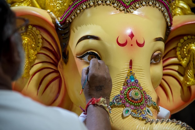 Artista haciendo una estatua y da los toques finales a un ídolo del dios hindú Lord Ganesha en un taller de artista para el festival de Ganesha