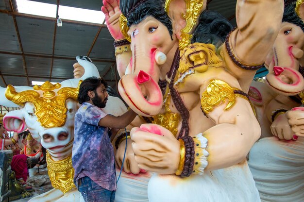 Artista haciendo una estatua y da los toques finales a un ídolo del dios hindú Lord Ganesha en un taller de artista para el festival de Ganesha