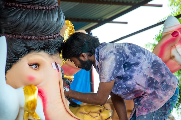 Artista haciendo una estatua y da los toques finales a un ídolo del dios hindú Lord Ganesha en un taller de artista para el festival de Ganesha