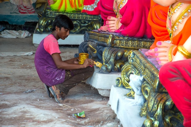 Artista haciendo una estatua y da los toques finales a un ídolo del dios hindú Lord Ganesha en un taller de artista para el festival de Ganesha