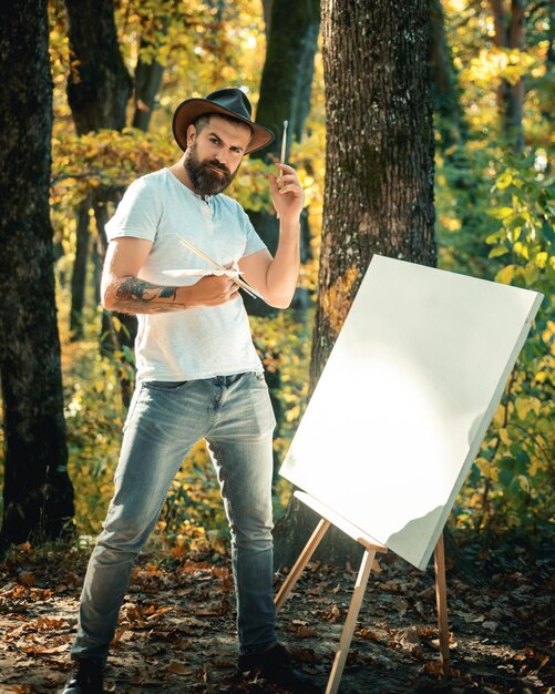 Artista hipster em um chapéu criando arte na pintura do conceito de arte da floresta na natureza começa uma nova imagem p