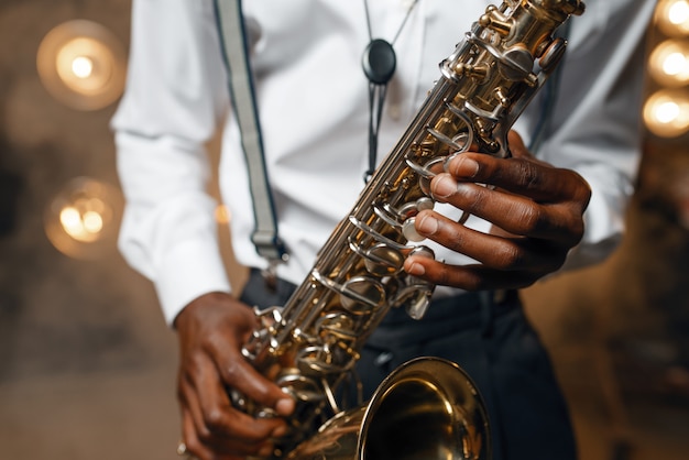 Artista de jazz masculino toca el saxofón en el escenario con focos. Jazzman negro actuando en la escena