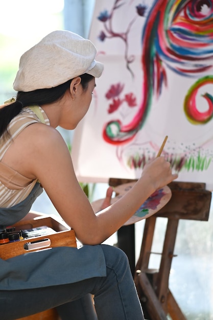 Artista jovem de vista lateral sentada em frente à tela e pintando com aquarela.