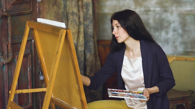 Artista jovem desenha imagens com tintas aquarela e pincel em tela de cavalete