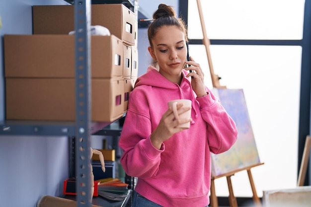 Artista jovem falando em smartphone bebendo café no estúdio de arte