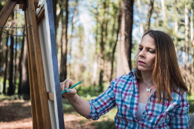 Artista jovem no cavalete pintura paisagem ao ar livre.