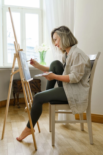 Artista jovem pintando sobre tela no cavalete em estúdio em casa