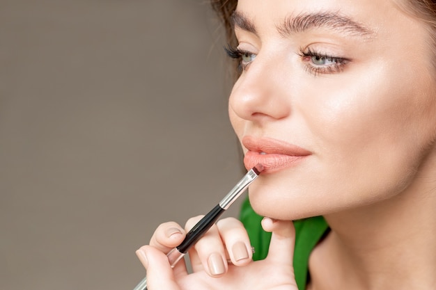 Artista de maquillaje aplica lápiz labial en la cara de una mujer hermosa, maquillaje en proceso.
