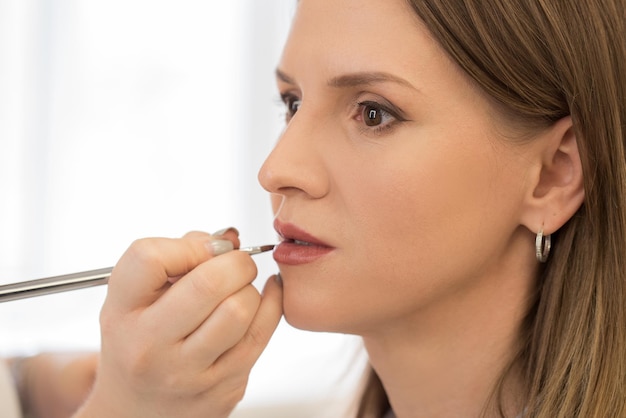 Artista de maquillaje aplica lápiz labial a una mujer hermosa