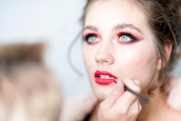 Artista de maquillaje aplica lápiz labial rojo Hermoso rostro femenino Mirada expresiva