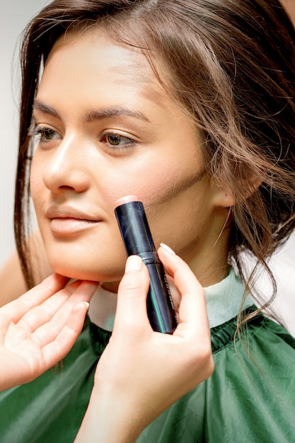 Artista de maquillaje aplicando crema rubor stick en la mejilla de la mujer