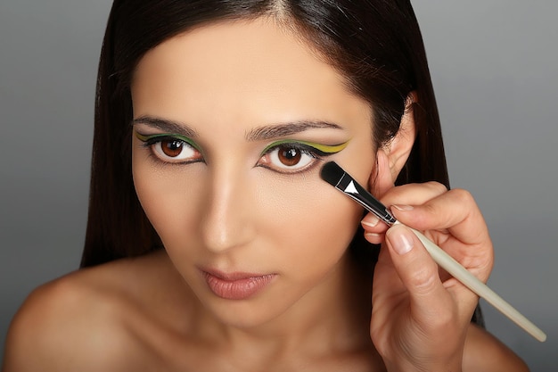 Artista de maquillaje aplicando maquillaje en ojos modelo sobre fondo gris