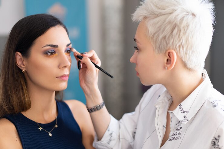 Foto artista de maquillaje aplicando sombra de ojos en color base brillante.