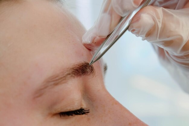 Un artista de maquillaje arranca las cejas de una mujer con una pinza Hermosas cejas gruesas en primer plano