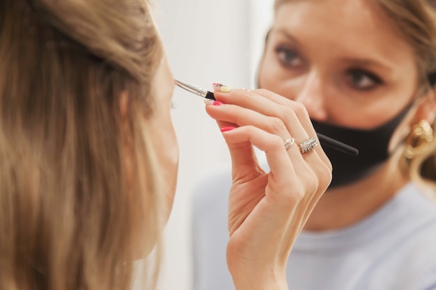 Artista de maquillaje femenino forma linda joven en salón de belleza. Atención al cliente en salón interior para crear una imagen sorprendente. Asistente de creación de maquillaje de trabajo. Concepto de satisfacción de la medida. Copia espacio