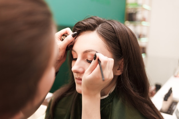 El artista de maquillaje hace maquillaje de cejas para su cliente. Procedimiento de dibujo de cejas